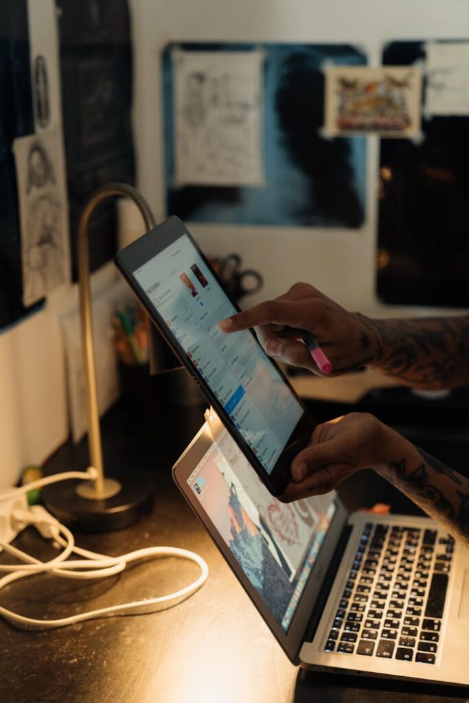 Person navigating a digital tablet while using a laptop in a creative indoor workspace.